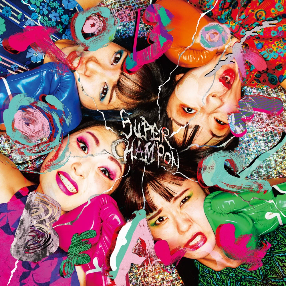 Faces of four Japanese women wearing brightly colorful makeup and clothing. They’re lying down in a circle with scrunched up faces from boxing gloves as if being punched. Each boxing glove is a different color, matching a clothing and makeup color theme for each. There are various painted shapes and splatters overlaid, and the record title is in the center, set with an electricity style font.