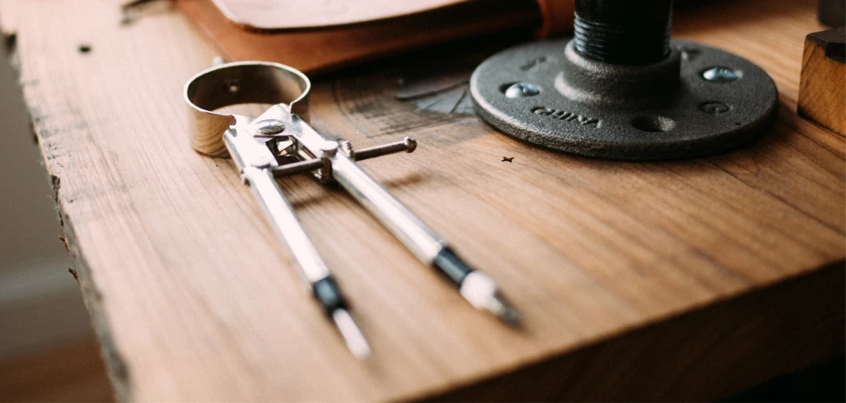 Drafting compass on a rustic wooden table that's turned upside down.