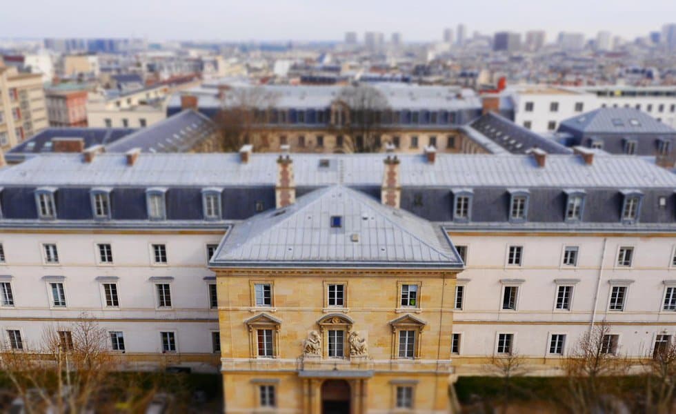 Four story building of old architecture, shaped in a square with an open courtyard, with Paris on the horizon behind it.